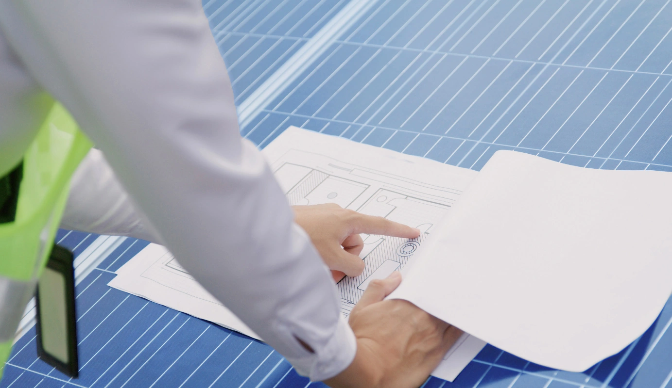 Person mit Warnweste zeigt auf technische Zeichnungen auf einem blauen Tisch Person mit Warnweste zeigt auf technische Zeichnungen auf einem blauen Tisch